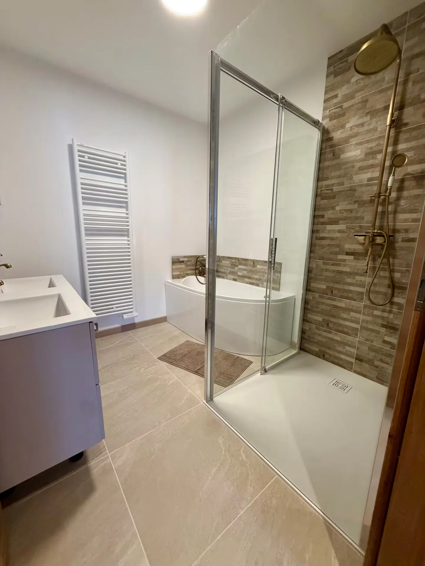 La salle de bain travertin : baignoire, grande douche et robinetterie laiton