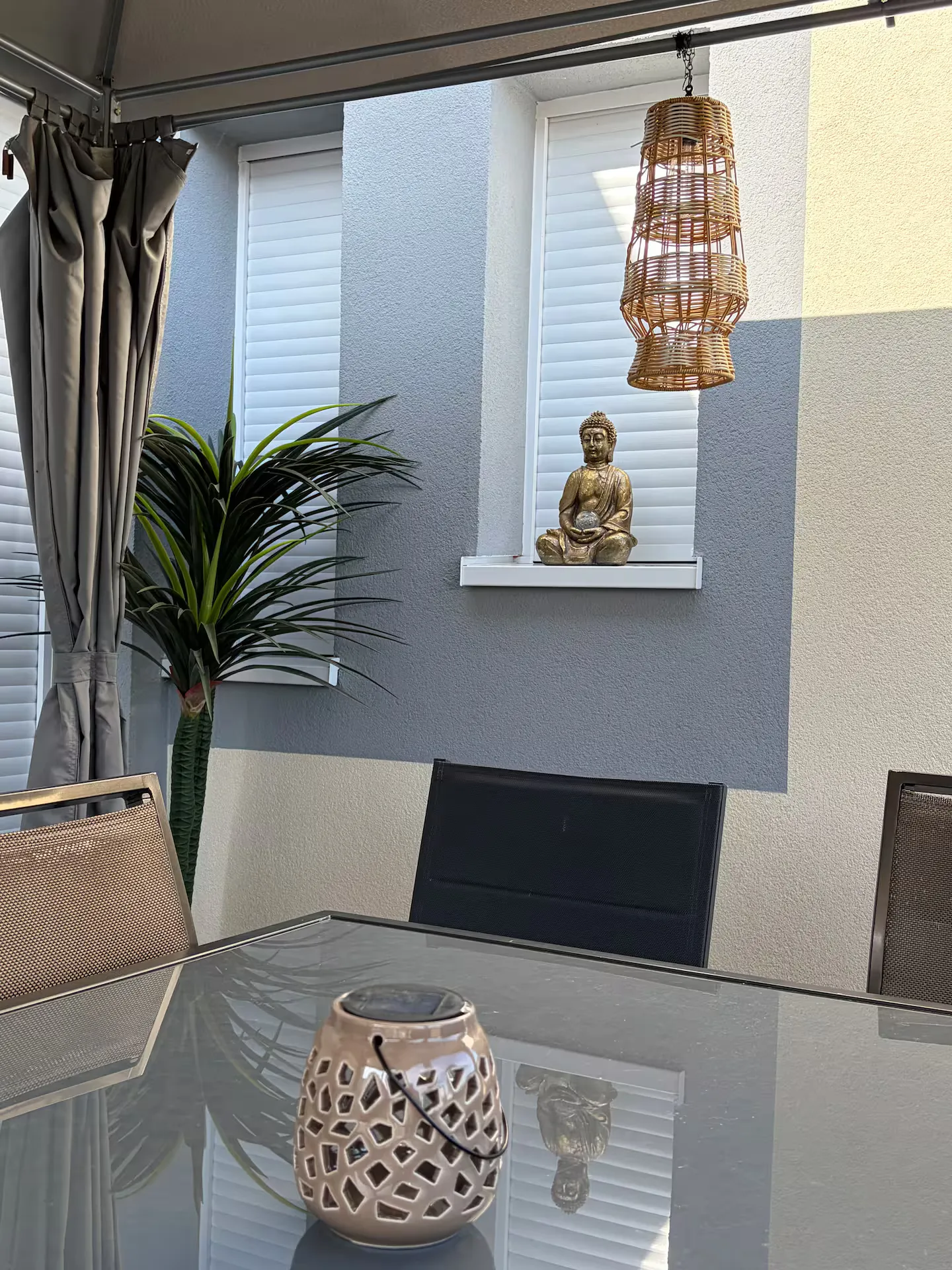 Sous la pergola : lanterne en rotin, bouddha doré sur l’appui de fenêtre
